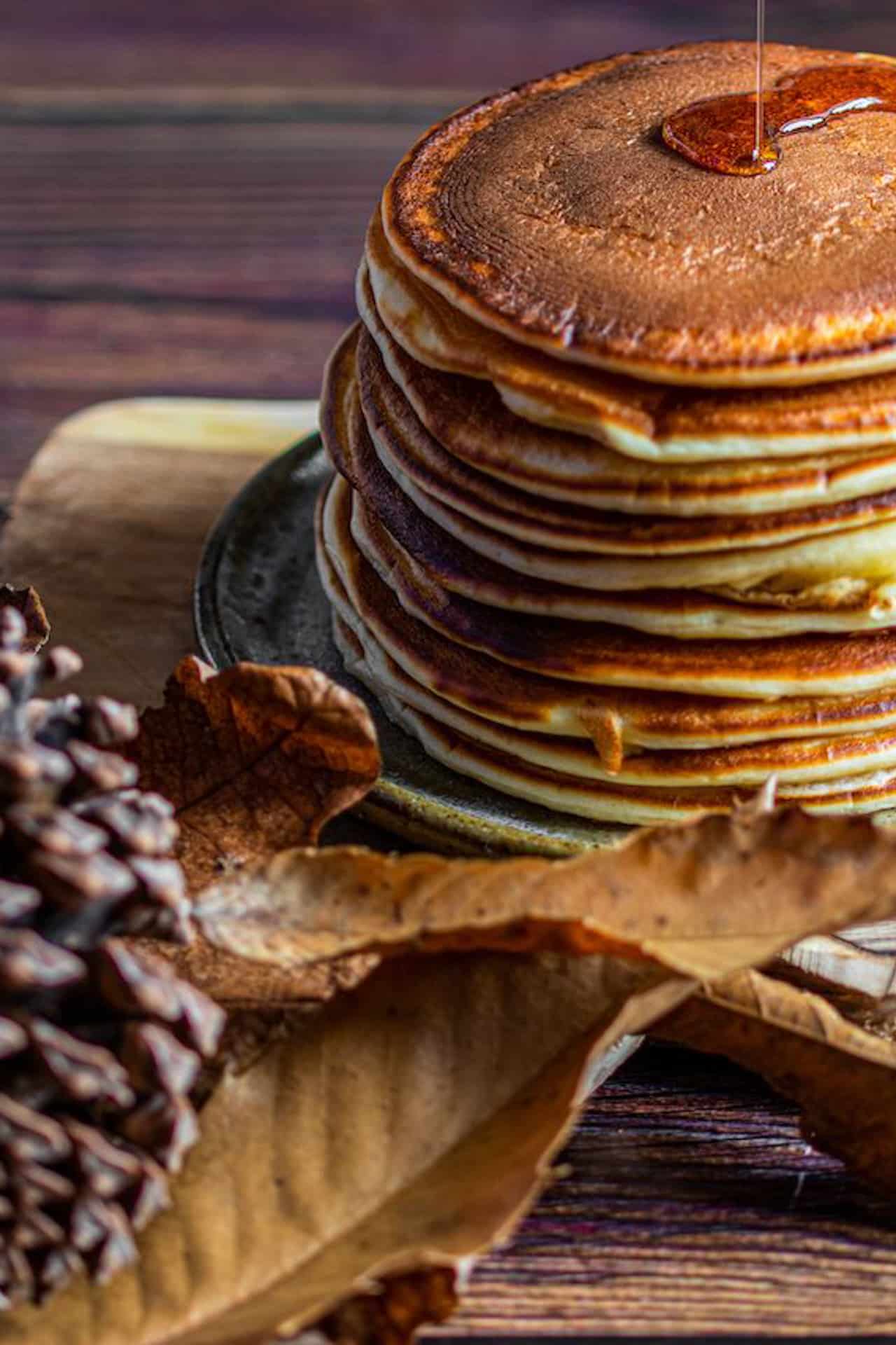 Syrup being poured on stack of pancakes on wooden board on rustic background with leaves rotch jones duff house and garden museum